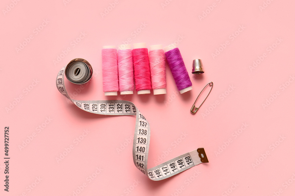 Thread spools, thimble, measuring tape and safety pin on color background