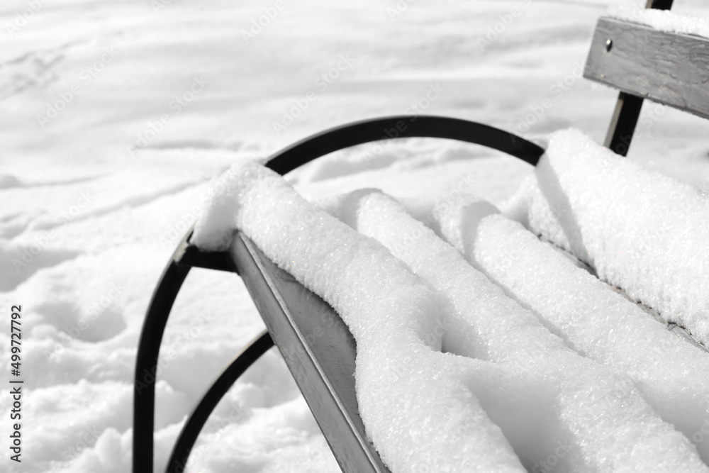 Wooden bench covered with snow in winter park, closeup