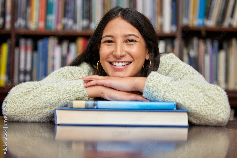 Explore and achieve. Shot of a young woman resting on a pile of books in a college library.