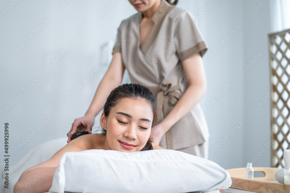 Asian young relaxing woman getting back massage therapy with hot stone