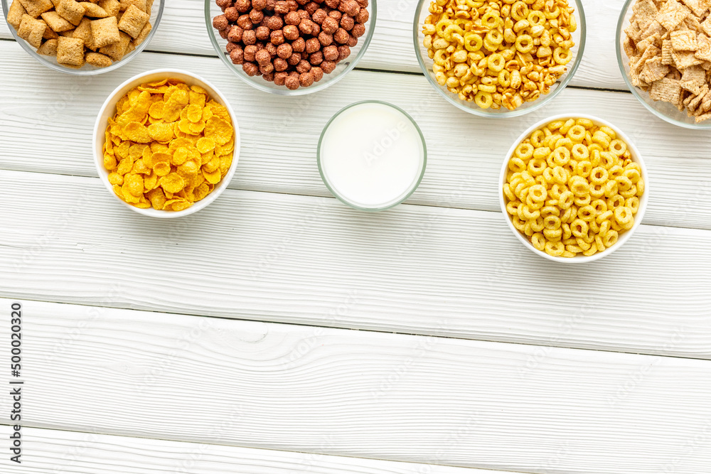 Various corn cereals in bowls and milk on white wooden background top view copyspace