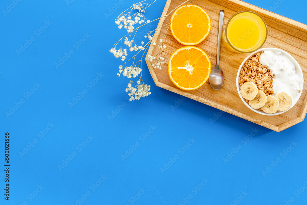 granola with banana slices and orange juice for breakfast on blue background top view copyspace