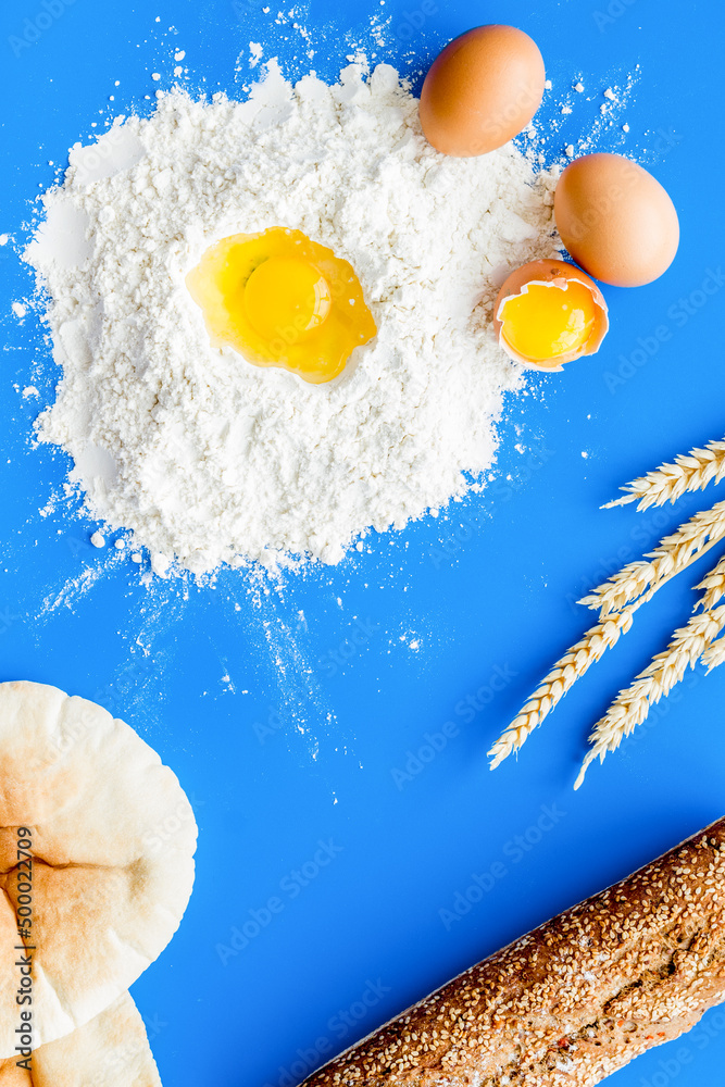 Baking background with eggs, flour and bread on blue desk. Top view.