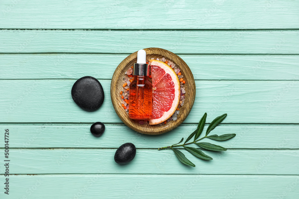 Composition with slice of grapefruit and bottle of essential oil on color wooden background