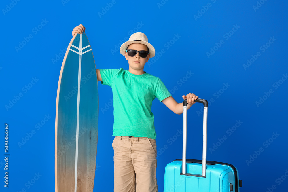 Cute little boy with suitcase and surfboard on color background