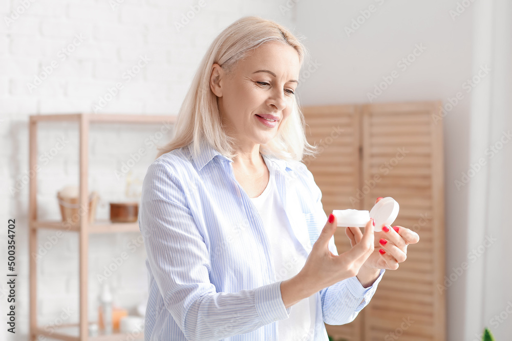 Beautiful mature woman with jar of cream in bathroom