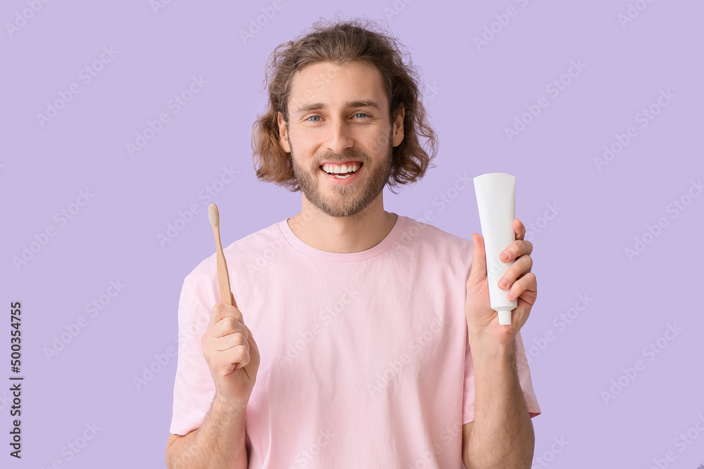 Handsome young man with tooth brush and paste on lilac background