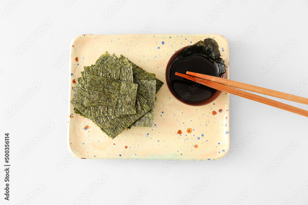 Plate of tasty seaweed sheets and bowl with soy sauce on light background