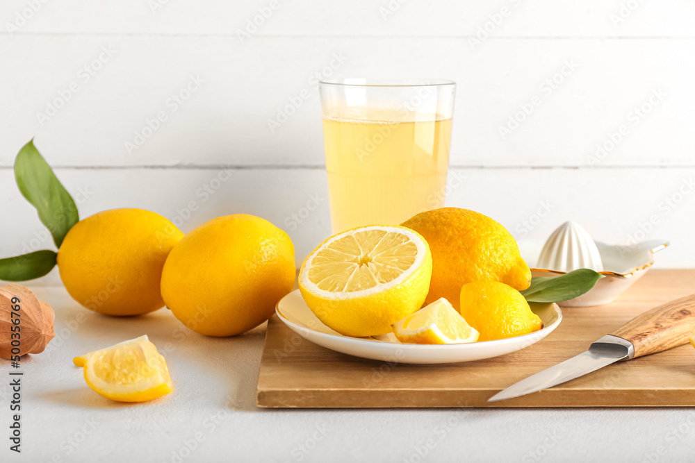 Wooden board with ripe lemons and glass of juice on light table