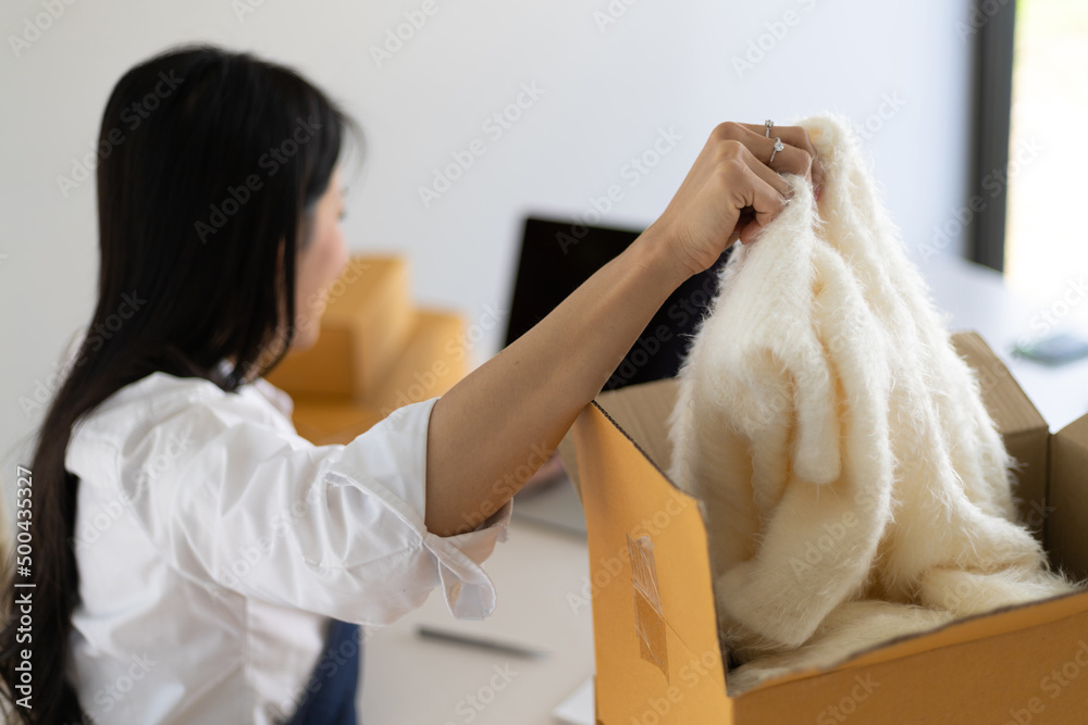 A female small ecommerce business owner is working on a laptop to check online orders and pack them 