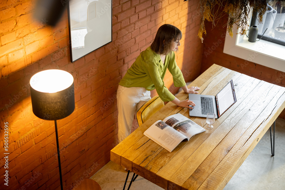 Woman works on laptop while sitting by the wooden table in cozy living room. Concept of remote work 