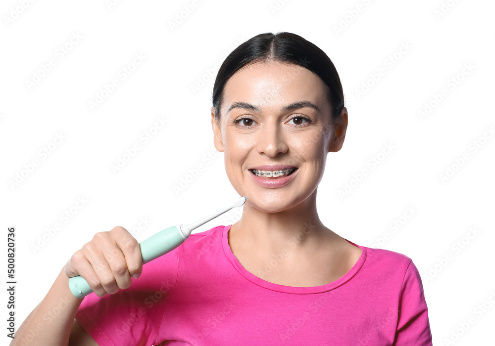 Beautiful woman with dental braces and electric toothbrush on white background