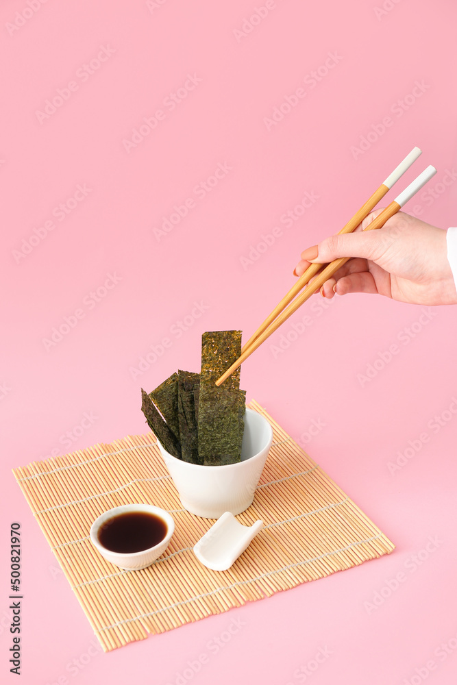 Woman eating tasty seaweed sheets on pink background