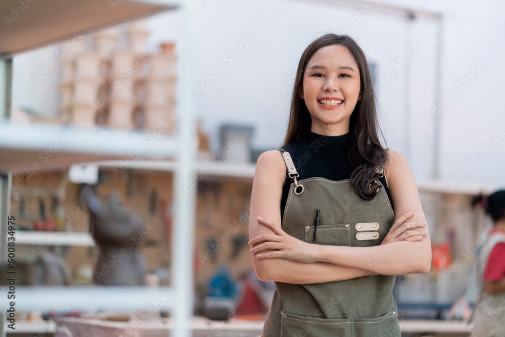 亚洲女陶艺家带着围裙，把她的粘土餐具放在架子上等待烘焙