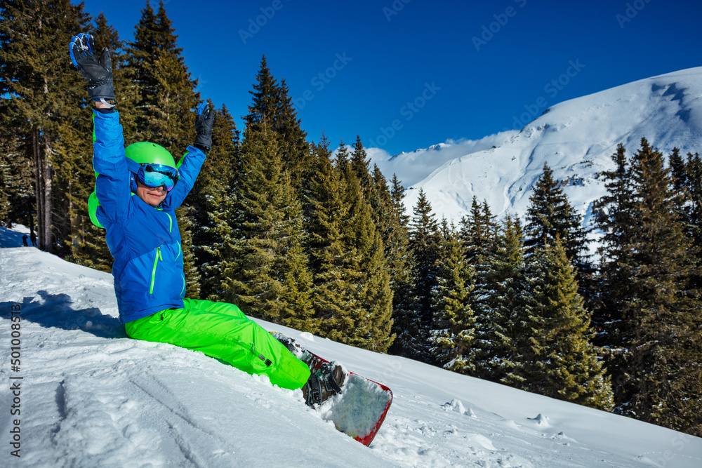 滑雪板上的孩子举起手坐在山上的雪上