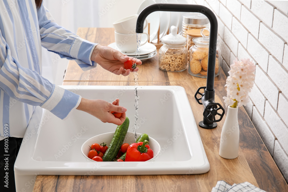 Woman washing fresh vegetables in kitchen sink