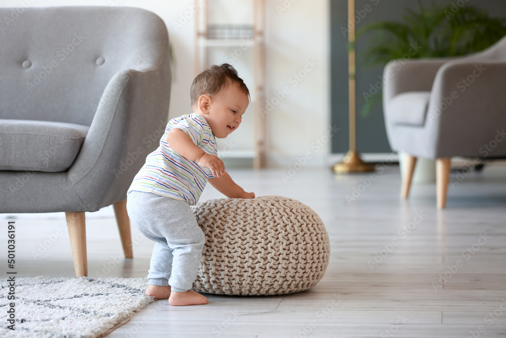 Little baby boy learning to walk near pouf at home