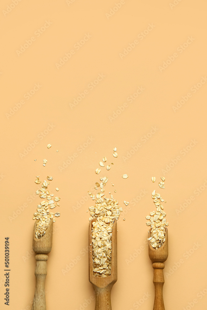 Scoops with raw oatmeal flakes on beige background