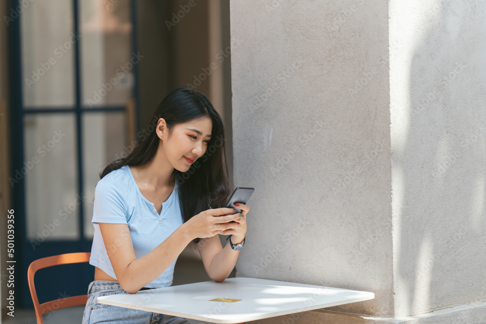 年轻的亚洲女人在咖啡店打电话，开心地笑着。