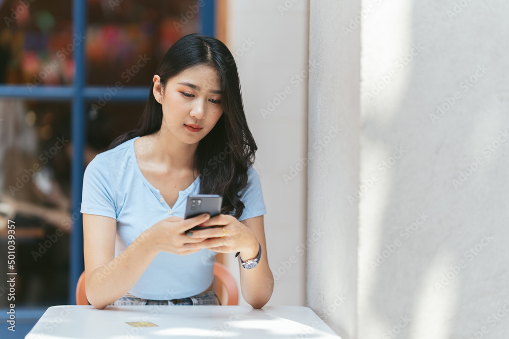 年轻的亚洲女人在咖啡店打电话，开心地笑着。