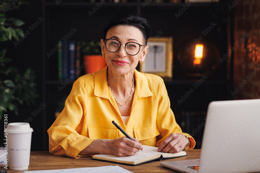 Middle aged businesswoman working at laptop,   take notes in home office