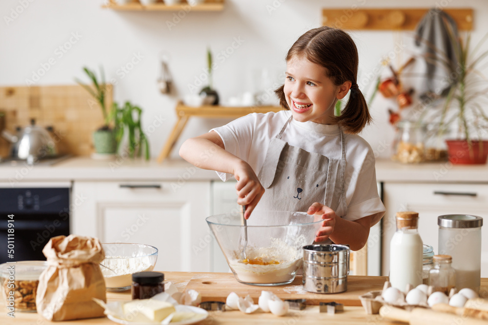 Happy child girl cooking pastry in kitchen