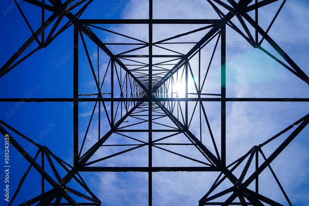 High voltage tower on blue sky background. Dramatic point of view with electricity pylon against blu