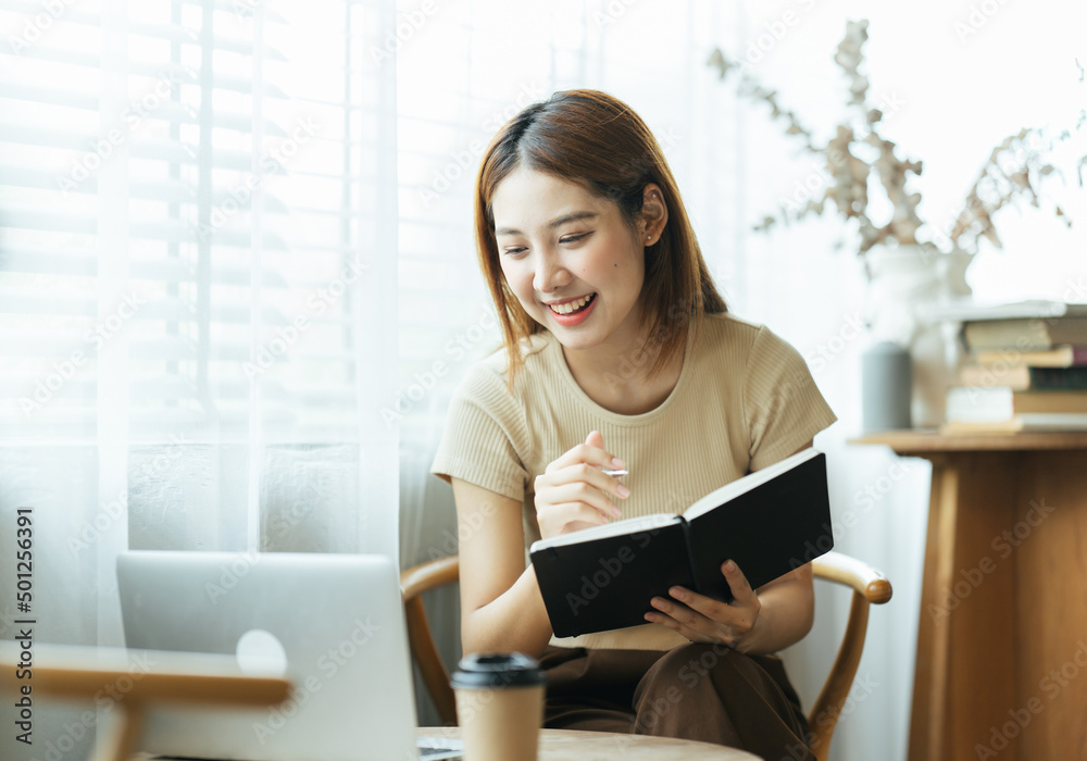 亚洲年轻女性在咖啡馆用笔记本电脑和财务报告工作的肖像。