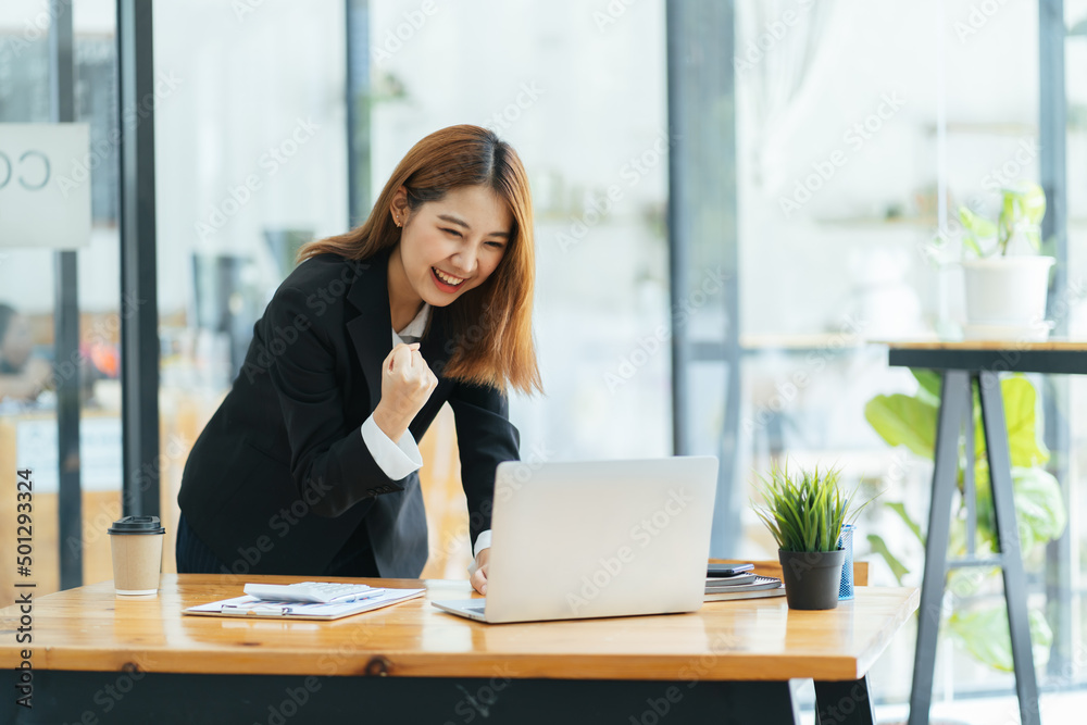 年轻女性拿着笔记本电脑在家办公时表达兴奋，兴奋的亚洲女性感到愉悦