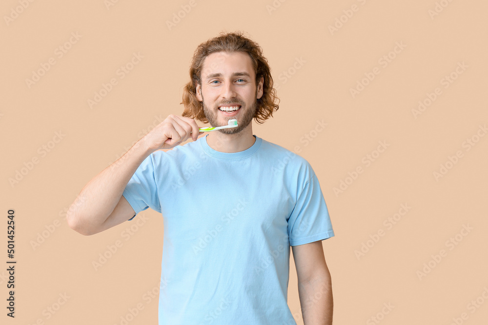 Young man brushing teeth on beige background