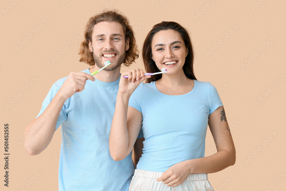 Young couple brushing teeth on beige background