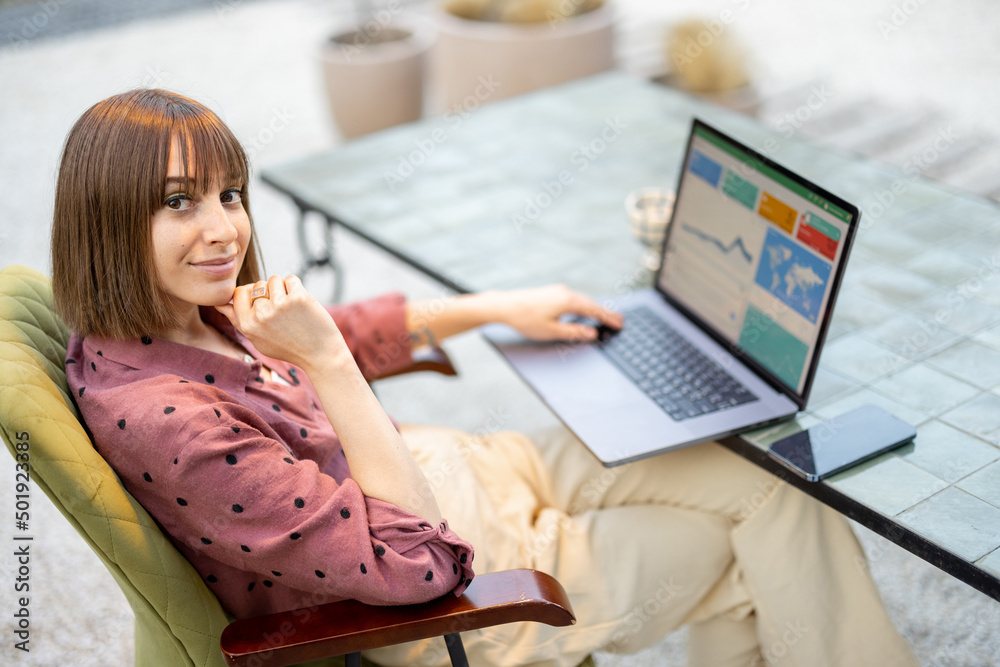 Portrait of a young woman works on laptop while sitting by the table outdoors. Concept of remote onl