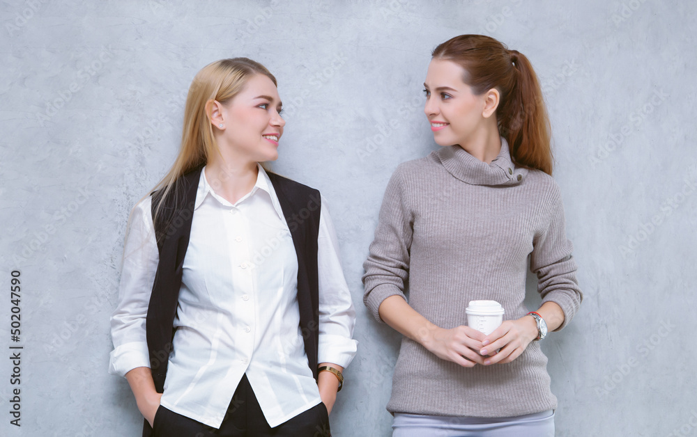 Cheerful young two women talking together during coffee break standing in modern office. Caucasian g