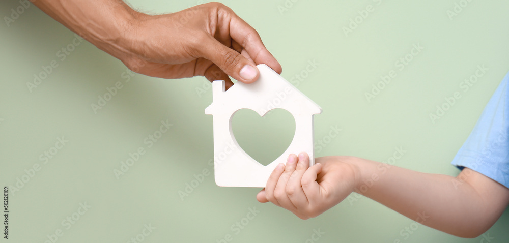 Hands of father and child with small figure of house on color background