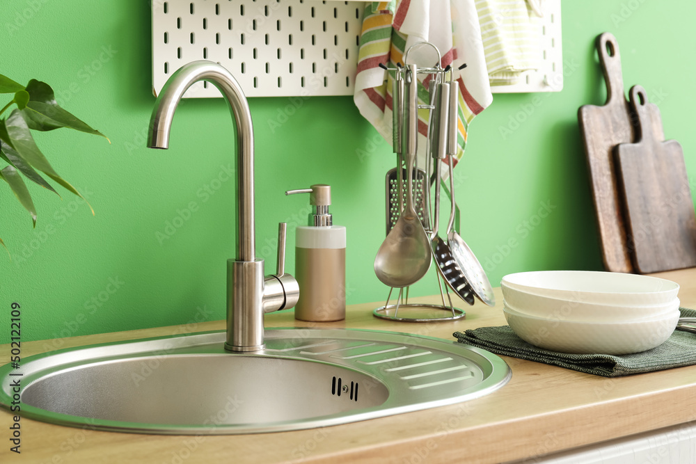 Wooden counter with silver sink and cookware near green wall in kitchen