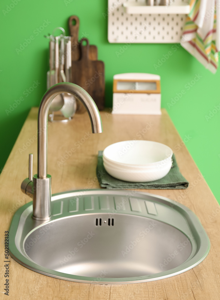 Wooden counter with silver sink near green wall in kitchen