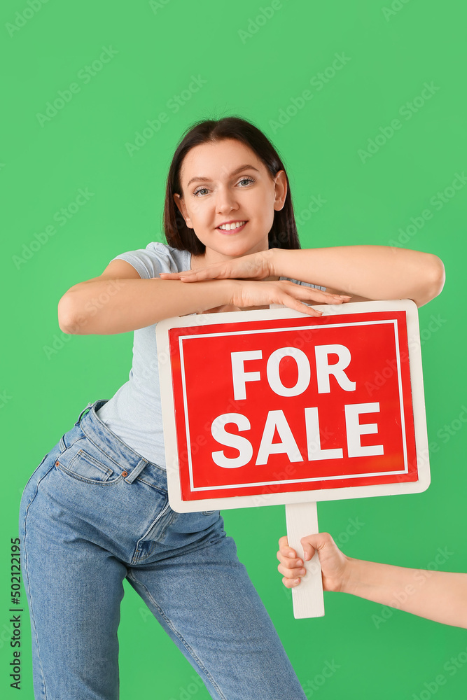 Young women with FOR SALE sign on green background