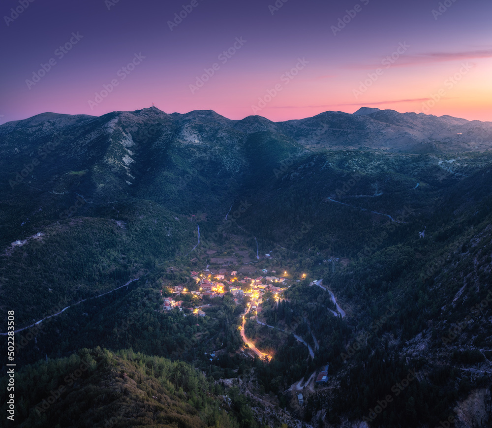 Small village on the mountain at night in summer. Aerial view. Beautiful landscape with city lights,