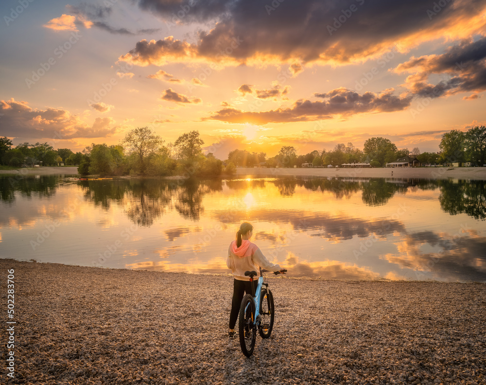 Woman riding a mountain bike near lake at sunset in summer. Colorful landscape with sporty girl, bic