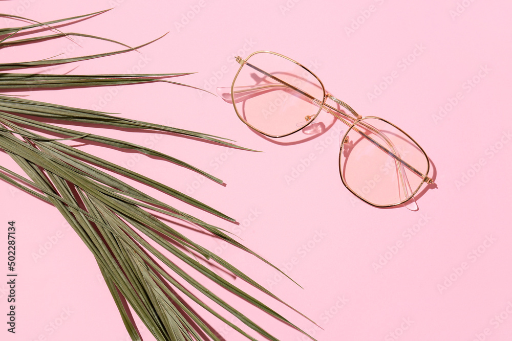 Stylish eyeglasses with tropical leaf on pink background