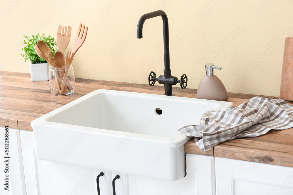 Counter with kitchen utensils, towel and ceramic sink near color wall