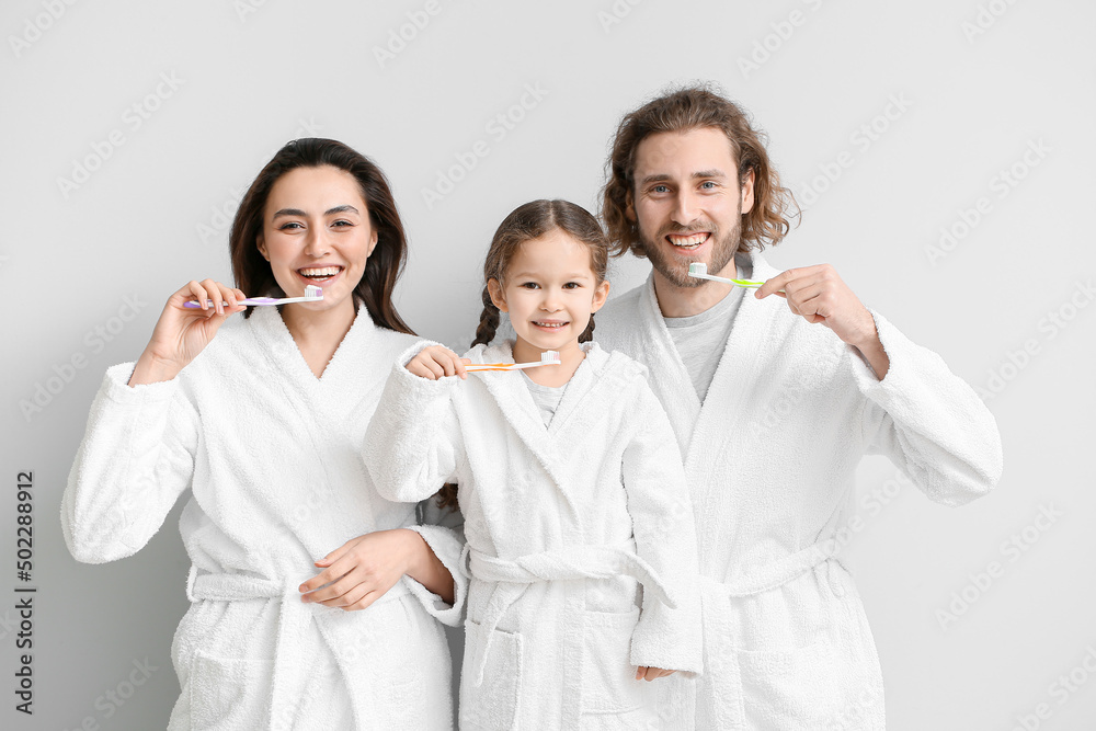 Little girl with her parents brushing teeth on light background