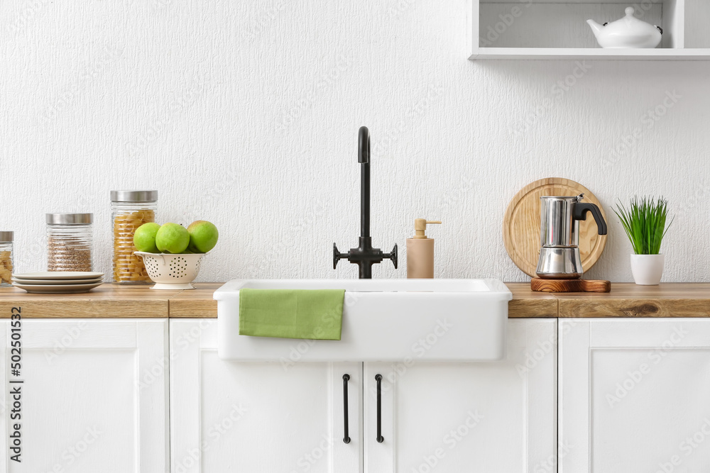 Counter with different utensils, fresh apple and ceramic sink near light wall