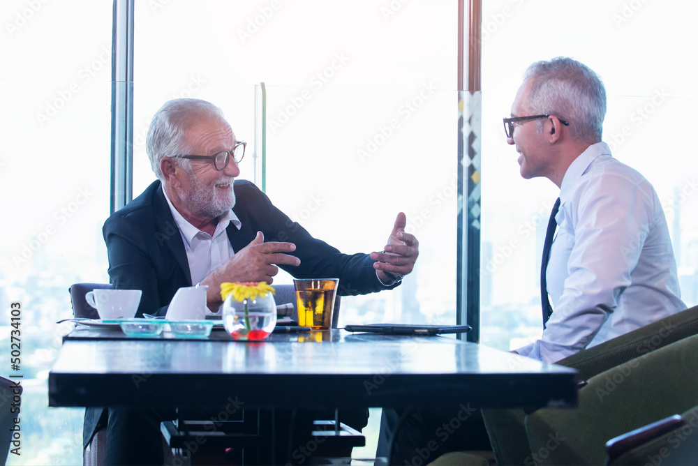 Senior businessman discuss information with a younger colleague in a modern business lounge.