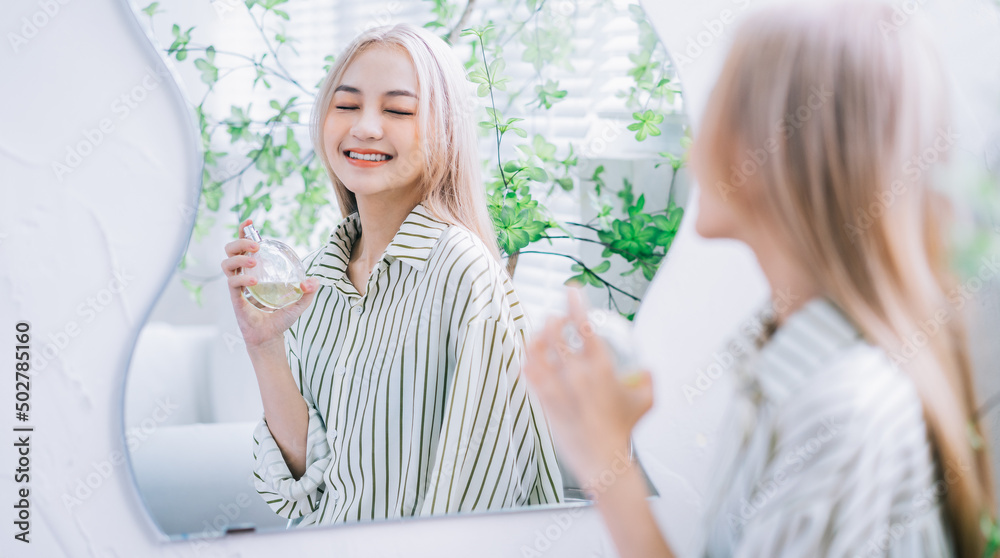 亚洲年轻女子在镜子前喷香水