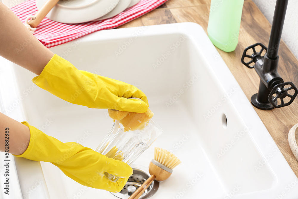 Woman in rubber gloves washing glass in sink, closeup