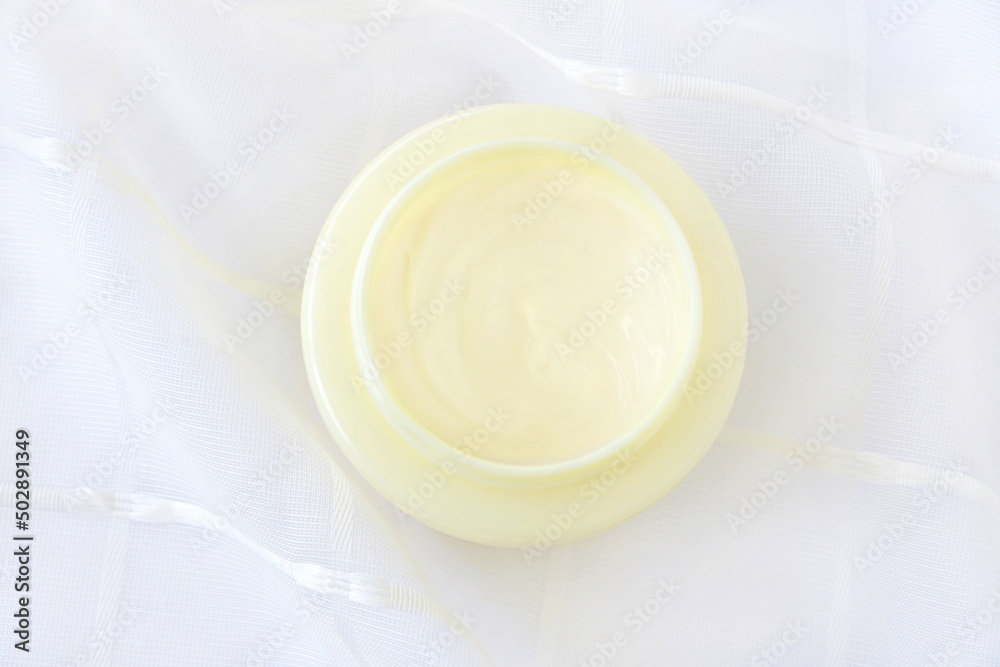 Close up yellow cream in plastic container on white fabric background, top view (flat lay style), lo