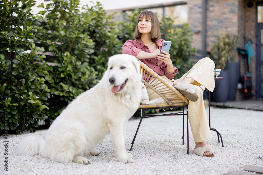 Young woman sitting relaxed with her huge white adorable dog, spending time together at backyard. Fr