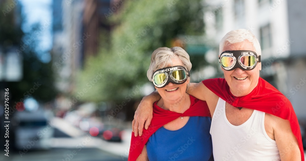 Portrait of caucasian senior couple wearing red capes and masks standing against buildings in city