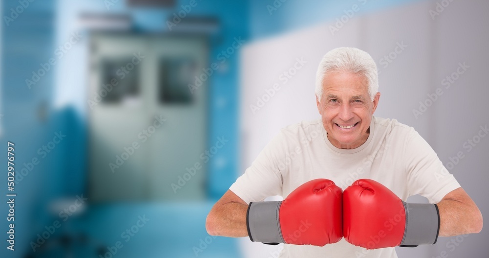 Portrait of smiling caucasian senior man wearing red boxing gloves while standing in health club